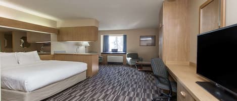 Habitación de hotel con una cama grande, un escritorio con computadora, televisión y ventana con cortinas.