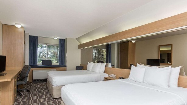 A hotel room with two beds, a desk, a chair, a TV, and a window with curtains. - Baymont Inn & Suites by Wyndham Anchorage Airport (Anchorage)