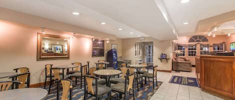 Un hall d’hôtel avec des tables et des chaises rondes, un comptoir d’accueil et un grand miroir au mur.