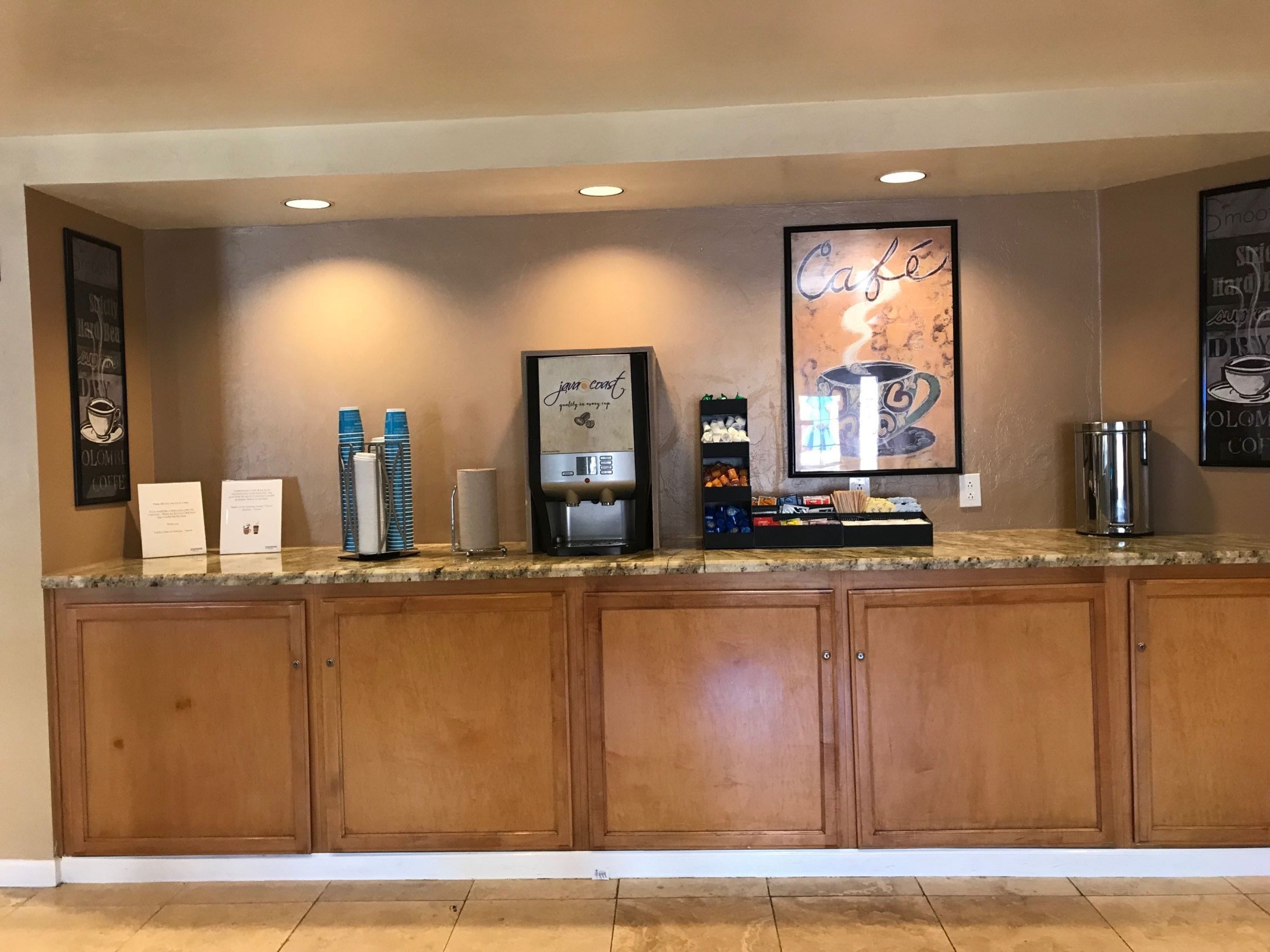 A coffee station with a coffee machine, cups, and a menu board.