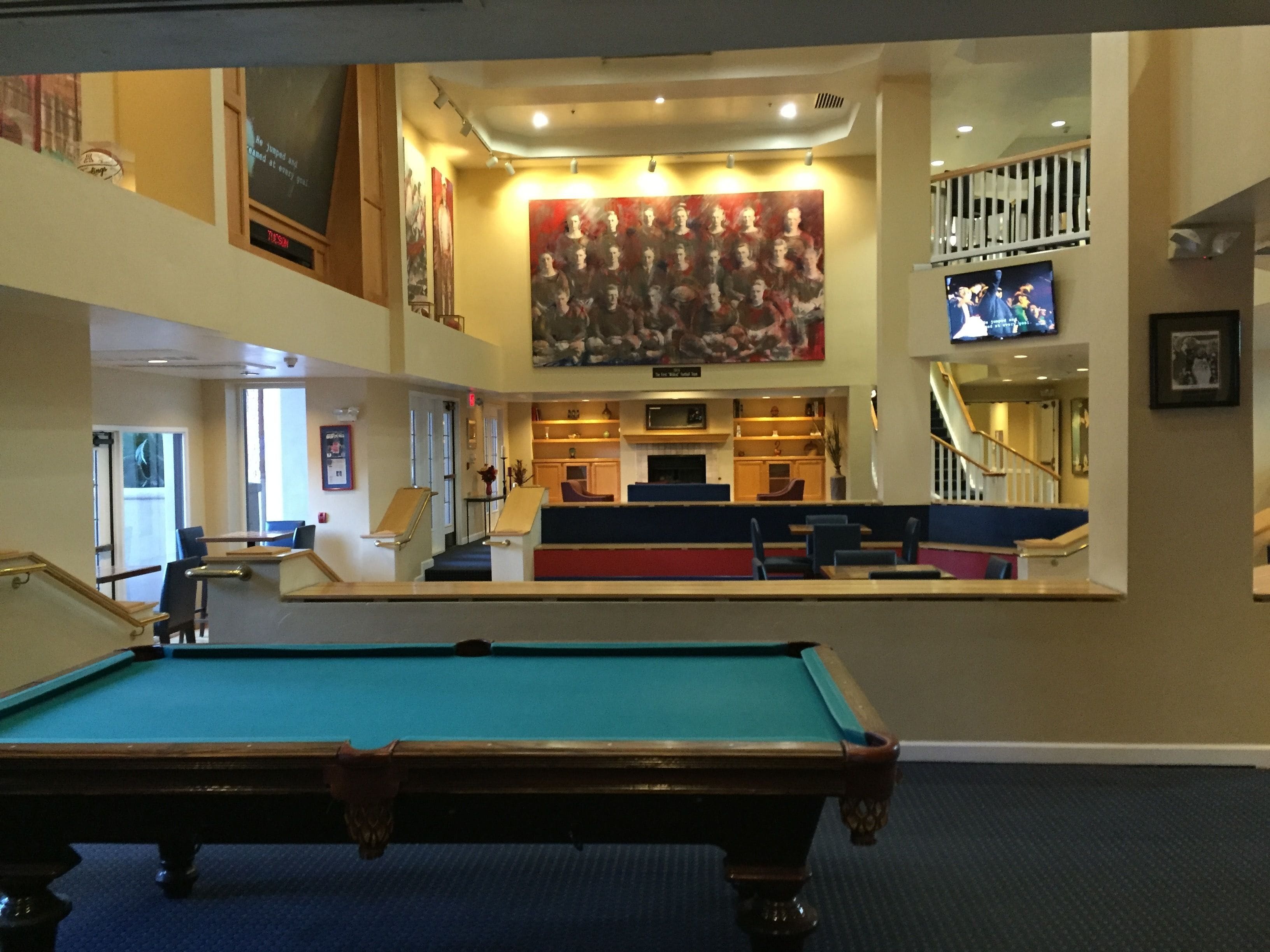 Une table de billard dans le hall d’un hôtel, avec un bar, des sièges et un escalier.