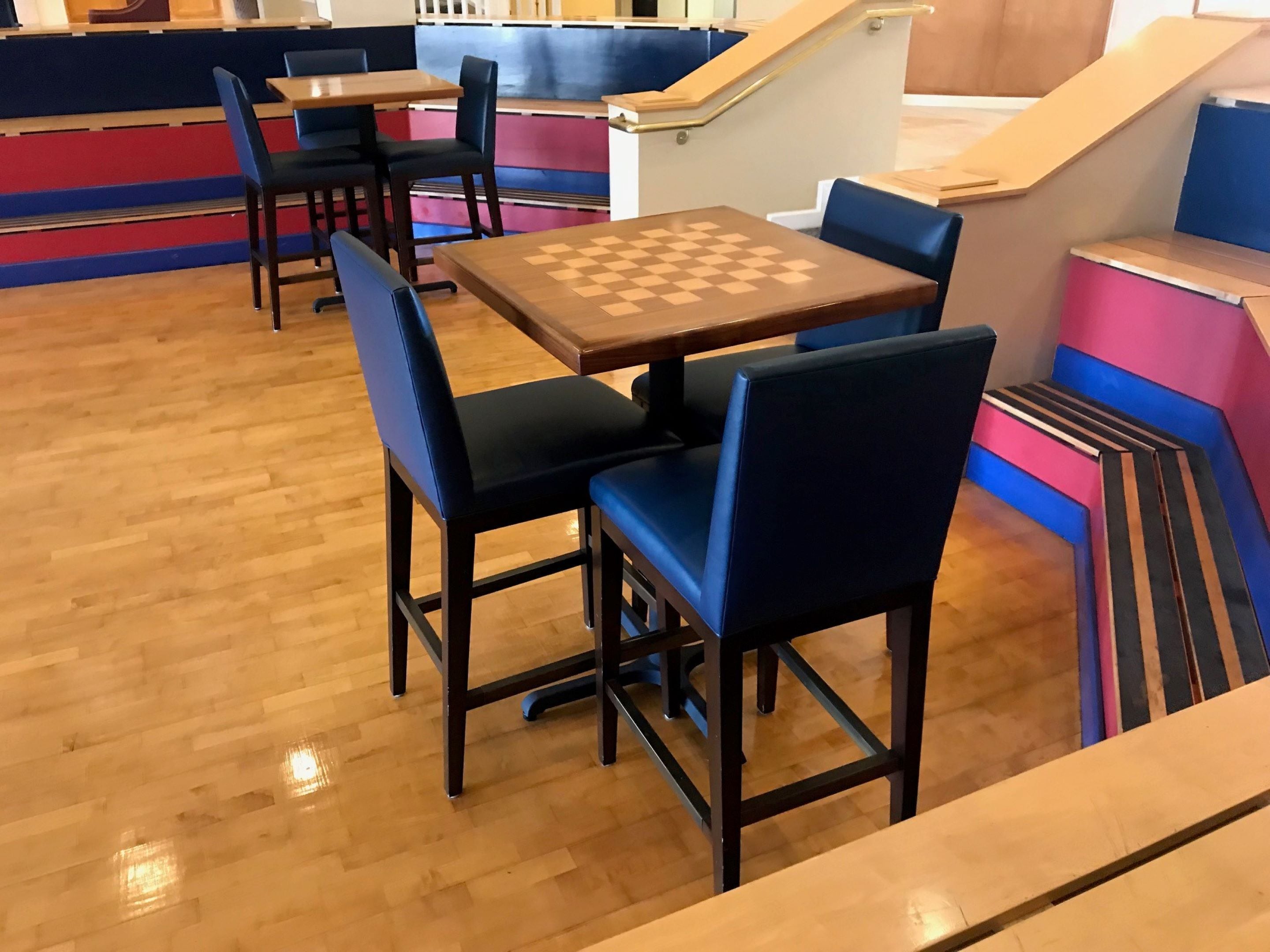 Une table d’échecs avec quatre chaises, un plancher en bois et un escalier agrémenté de touches de bleu et de rose.