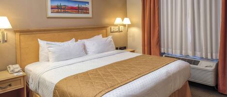 A hotel room with a bed, two bedside lamps, a nightstand with a phone, a painting on the wall, and a window with curtains.