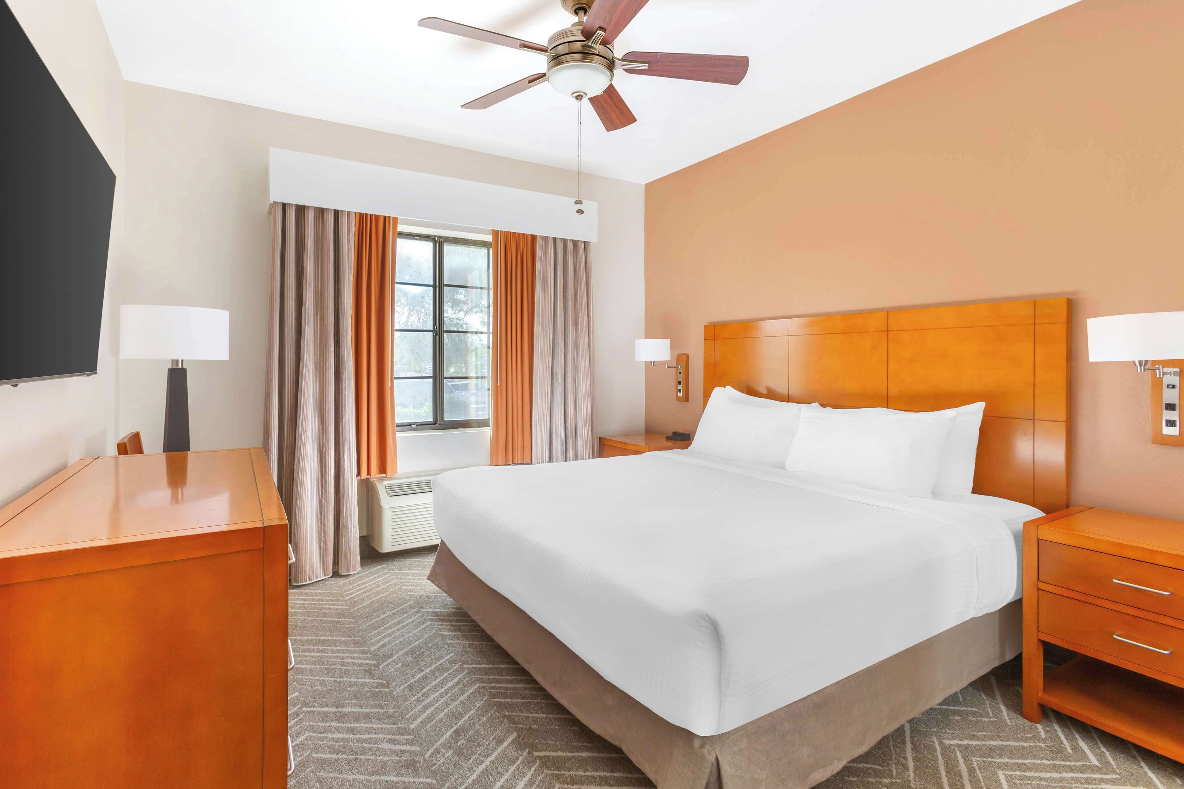A hotel room with a large bed, a ceiling fan, a TV, and a window with curtains.