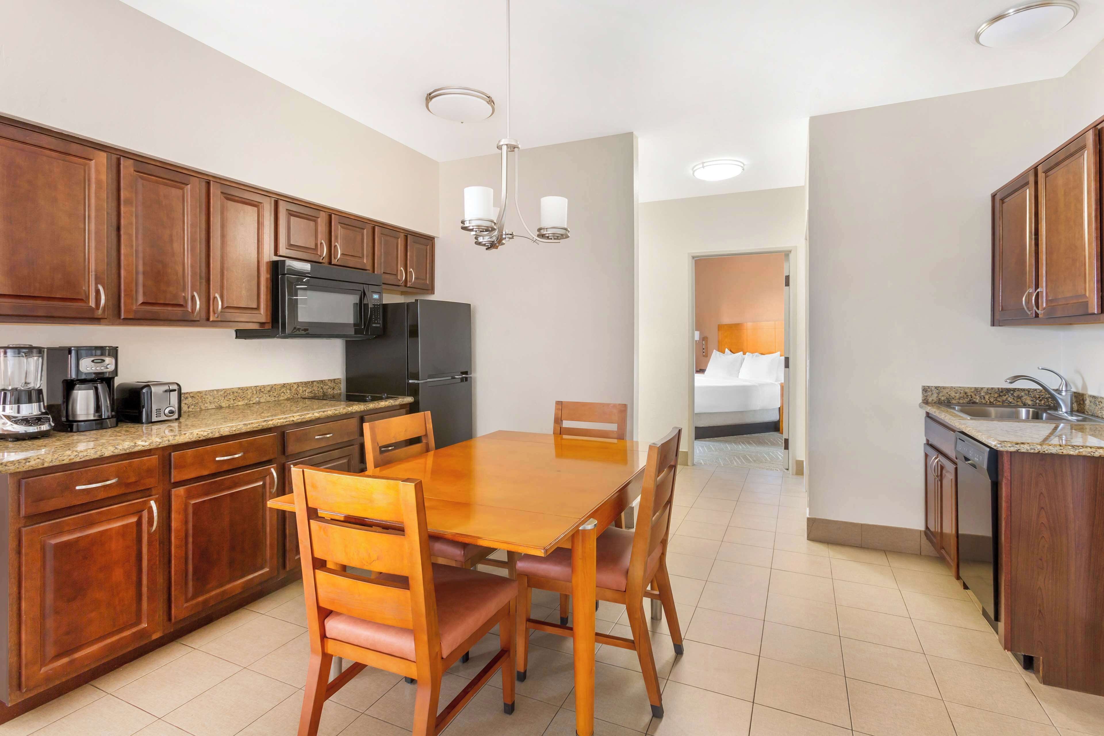 A modern kitchen with wooden cabinets, a granite countertop, a dining table with chairs, and a microwave.