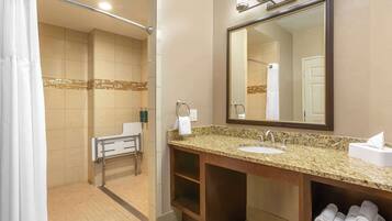 A modern bathroom with a granite countertop sink, a large mirror, and a towel rack.