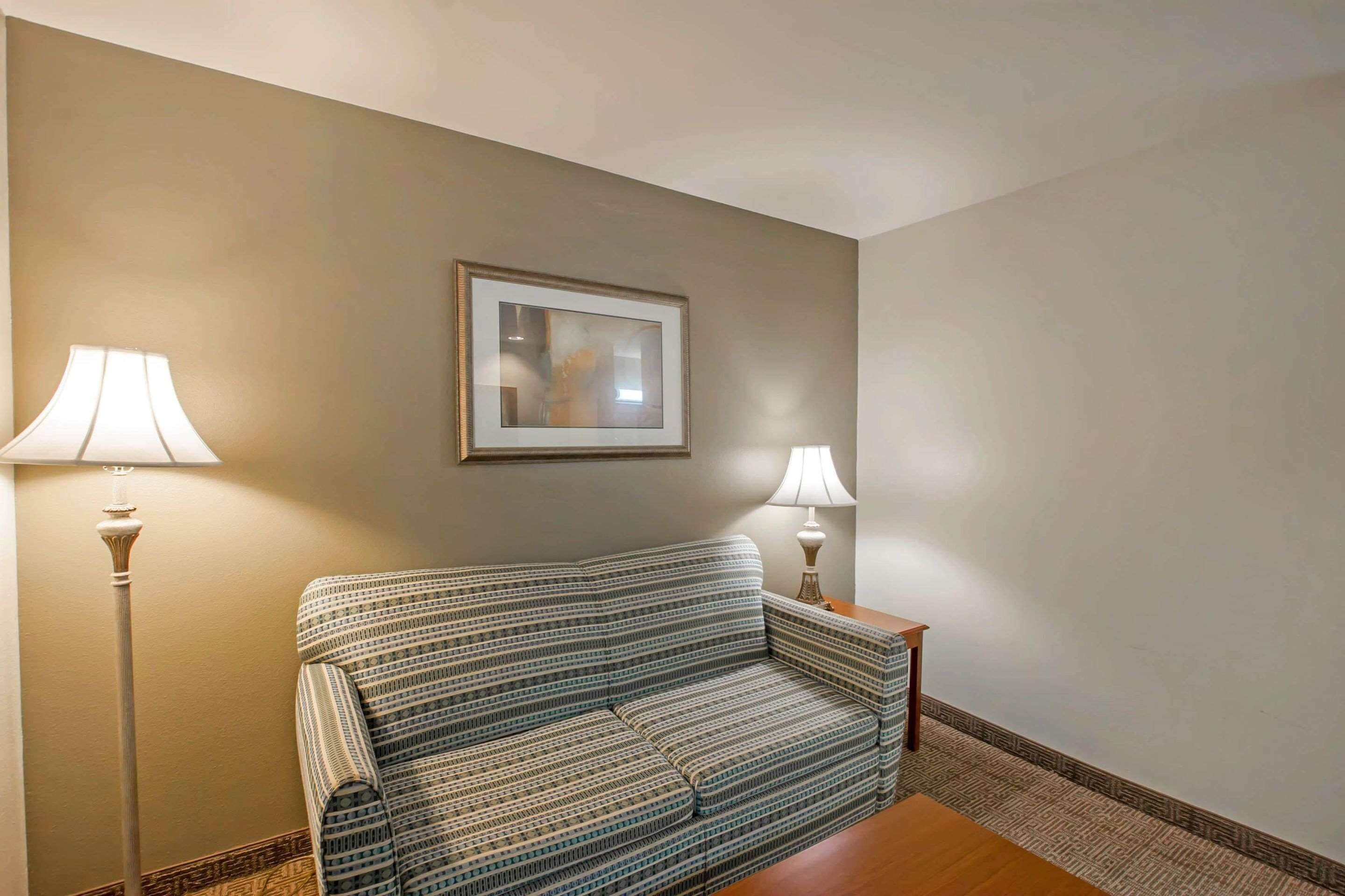 A room with a striped sofa, two floor lamps, and a framed picture on the wall.