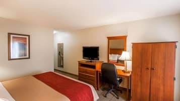 Una habitación de hotel con una cama, un escritorio con computadora, televisor, armario y un cuadro en la pared.