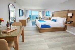 A hotel room with a large bed, a desk, a chair, a glass table, and a view of the ocean. - Divi Aruba Phoenix Beach Resort (Noord)