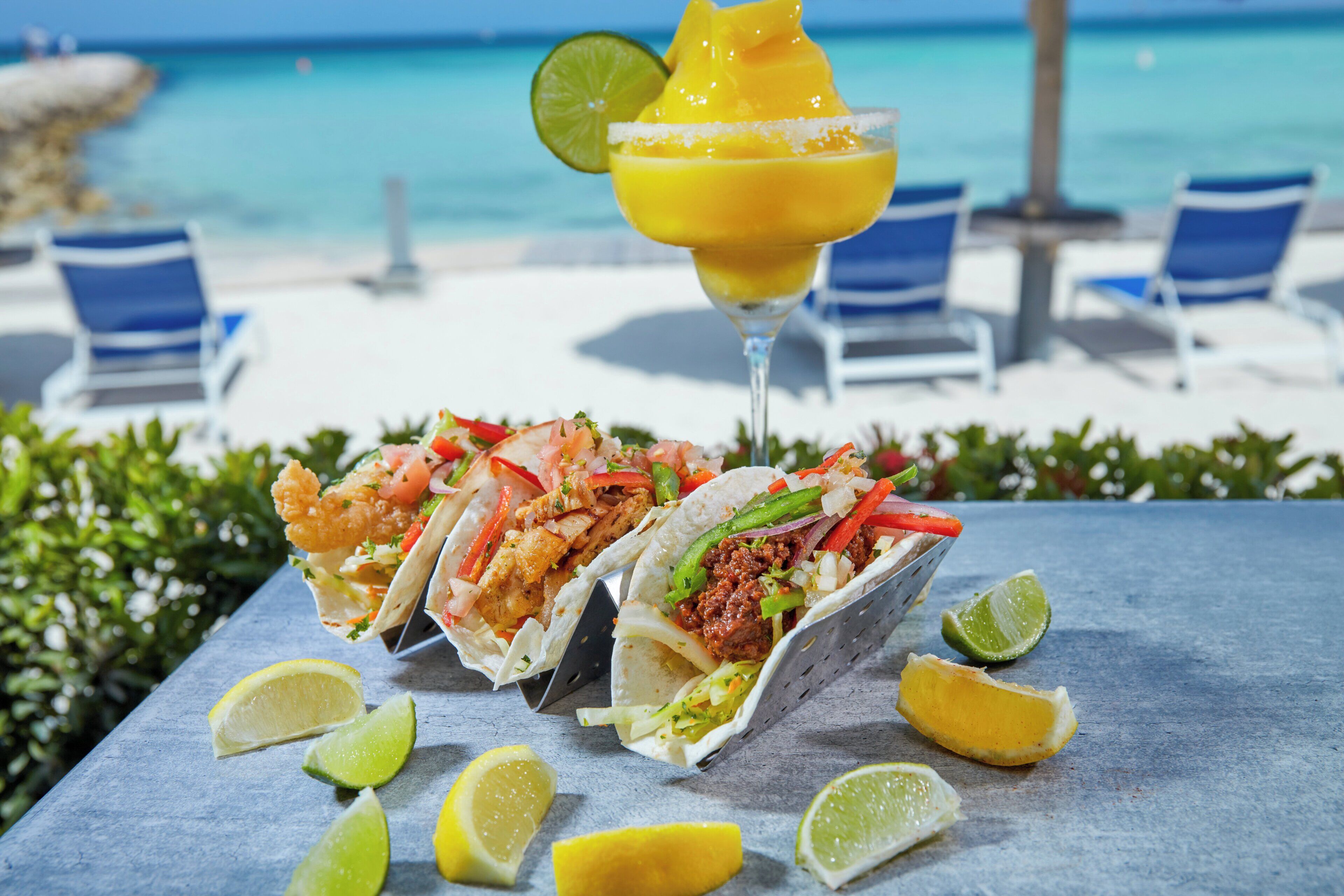 Une table avec trois tacos et un cocktail margarita, placée sur une table au bord de la plage.