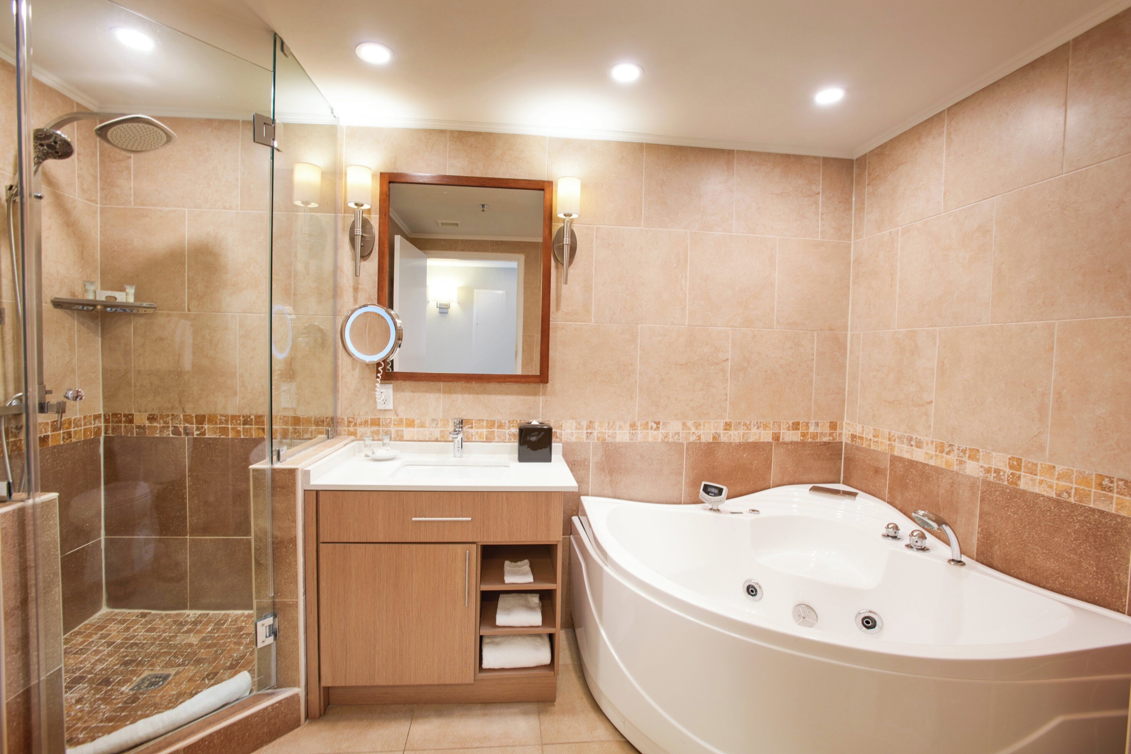 Un baño con ducha de vidrio, una bañera blanca y un tocador de madera con espejo.