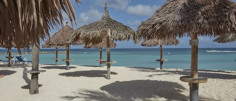 Uma praia com guarda-sóis de palha e espreguiçadeiras.