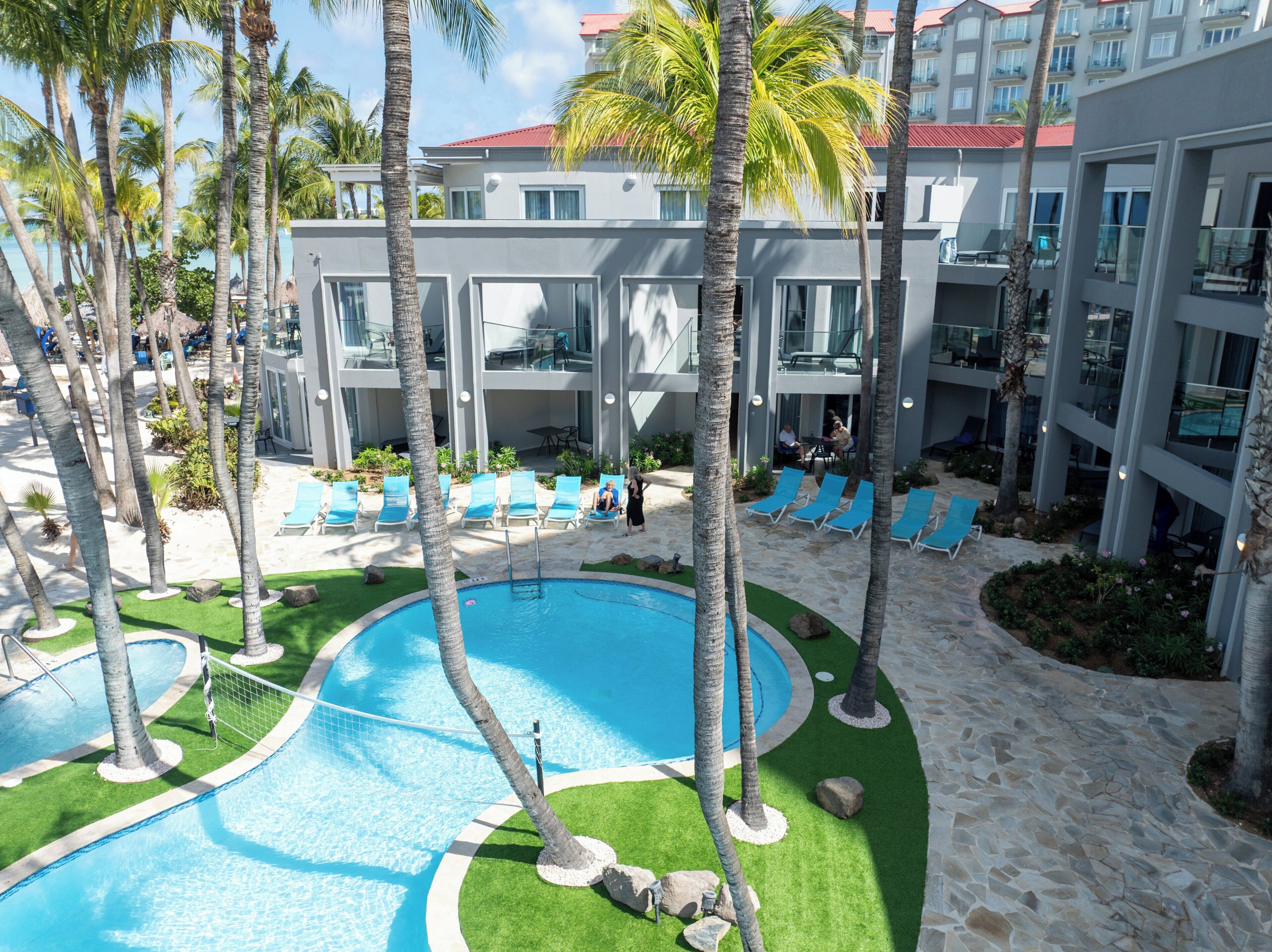 Un resort con piscina, palmeras y un edificio con balcones.