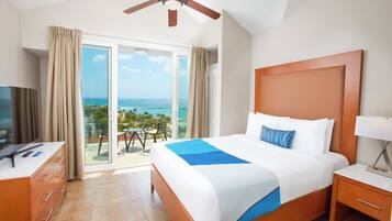 Habitación de hotel con cama, escritorio, televisor y balcón con vista al océano.
