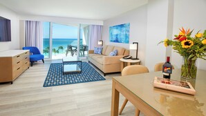 A modern hotel room with a glass table, a sofa, a blue armchair, a wooden dresser, and a view of the ocean. - Divi Aruba Phoenix Beach Resort (Noord)