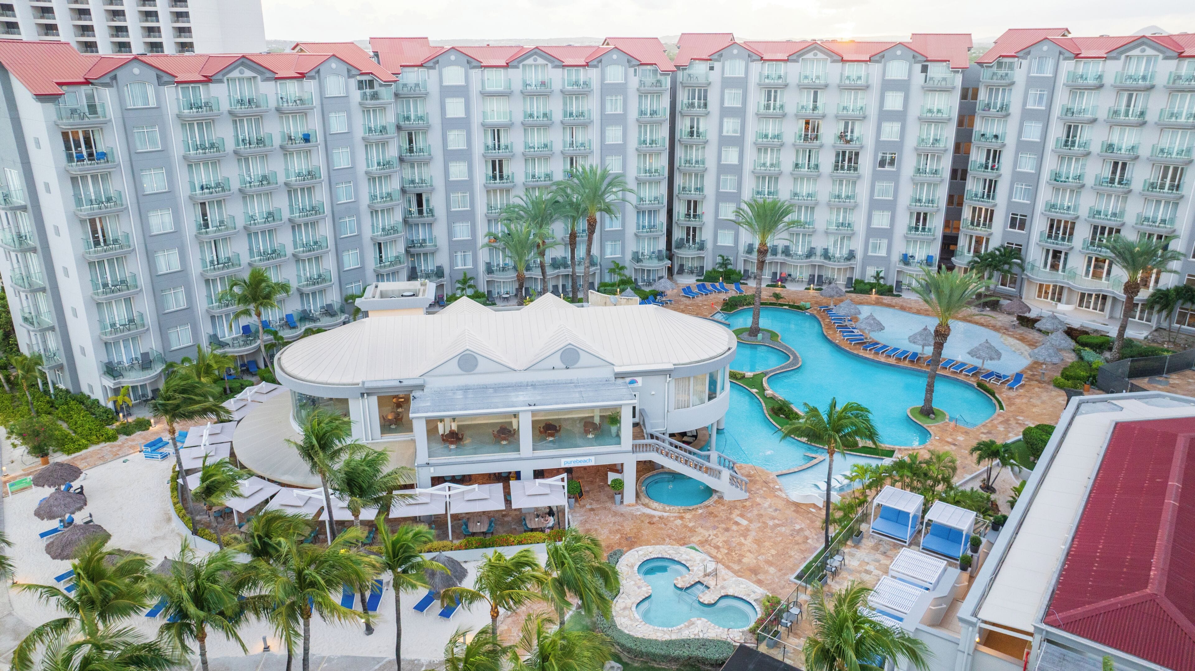 A hotel with multiple balconies, a pool area with lounge chairs, and a building with a curved roof.