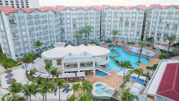 A hotel with multiple balconies, a pool area with lounge chairs, and a building with a curved roof.