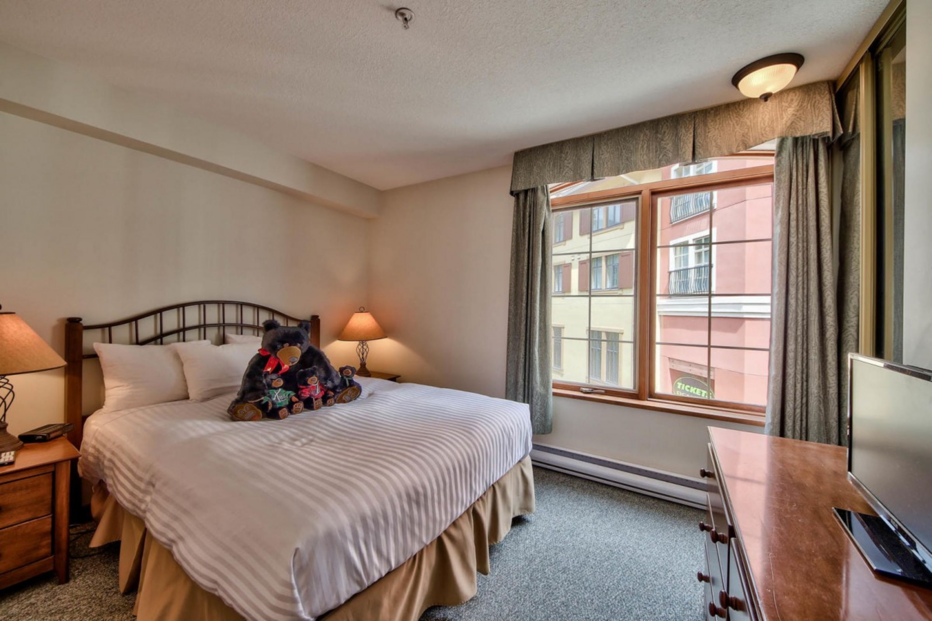 A hotel room with a bed, bedside lamps, a TV, and a window with curtains.