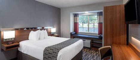 A hotel room with a large bed, bedside tables with lamps, a desk, a chair, a TV, and a window with curtains.