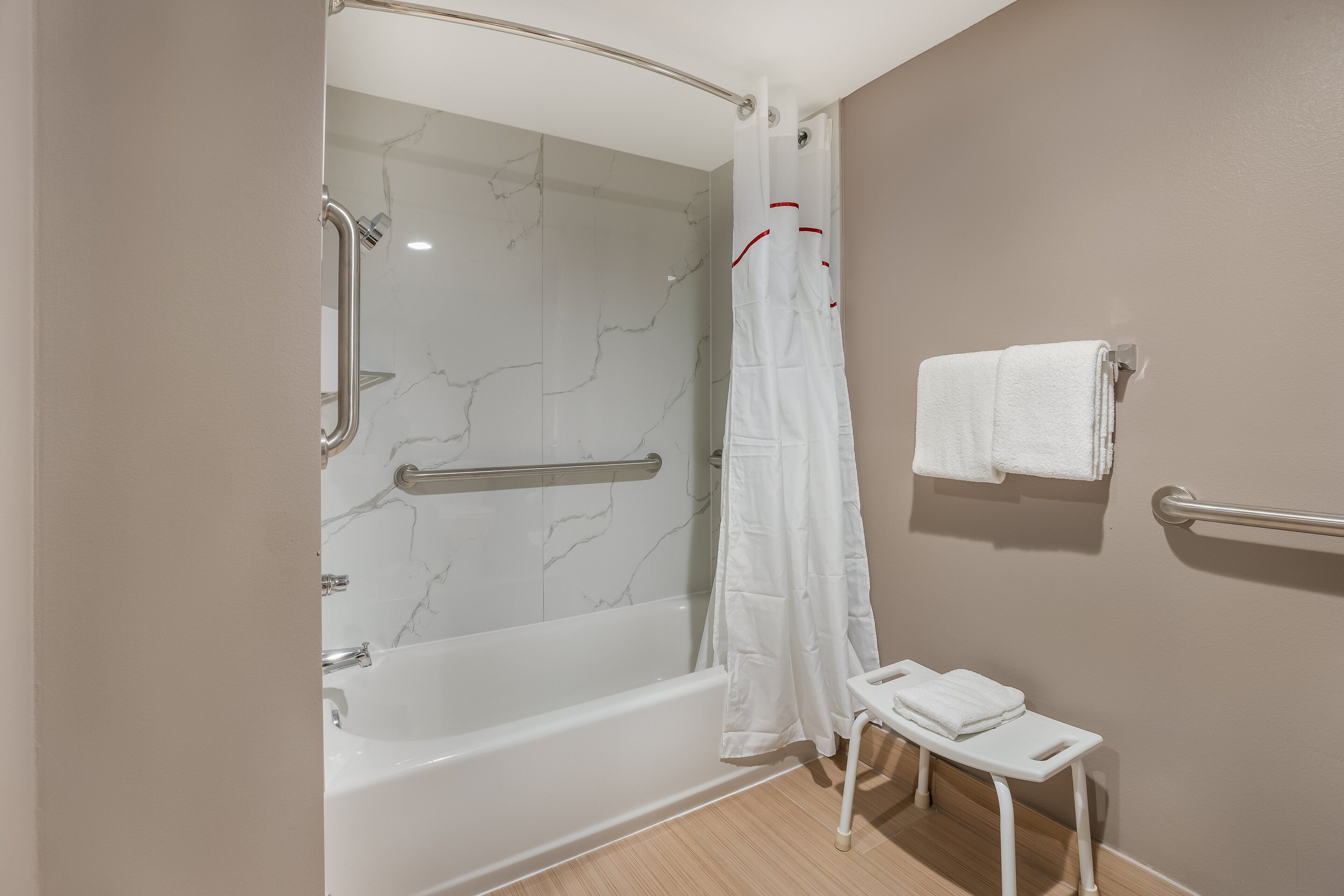 A bathroom with a shower, a bathtub, a small stool, and a towel rack.