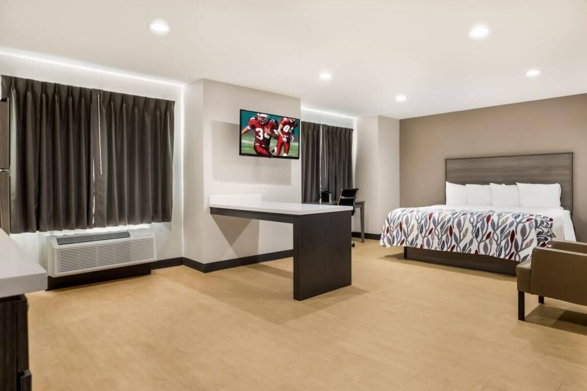 A modern hotel room with a bed, a desk, a TV, and a window with curtains.