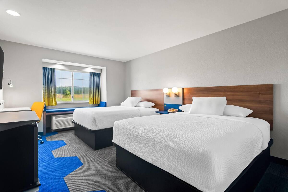 A hotel room with two beds, a desk, and a window with curtains.