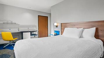 A hotel room with a large bed, a desk, a chair, and a nightstand with a lamp.