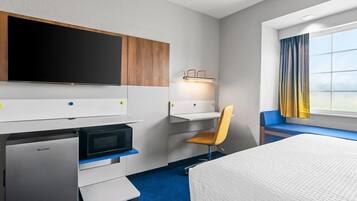 Una camera d'albergo con un letto, una scrivania con una sedia, una televisione, un forno a microonde e un piccolo frigorifero.