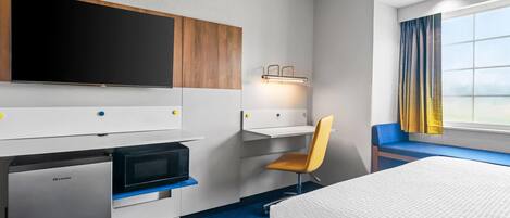 A hotel room with a bed, a desk with a chair, a television, a microwave, and a small refrigerator.