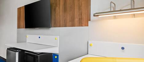 Una kitchenette compacta con microondas, un televisor de pantalla plana y un panel de madera sobre la encimera.