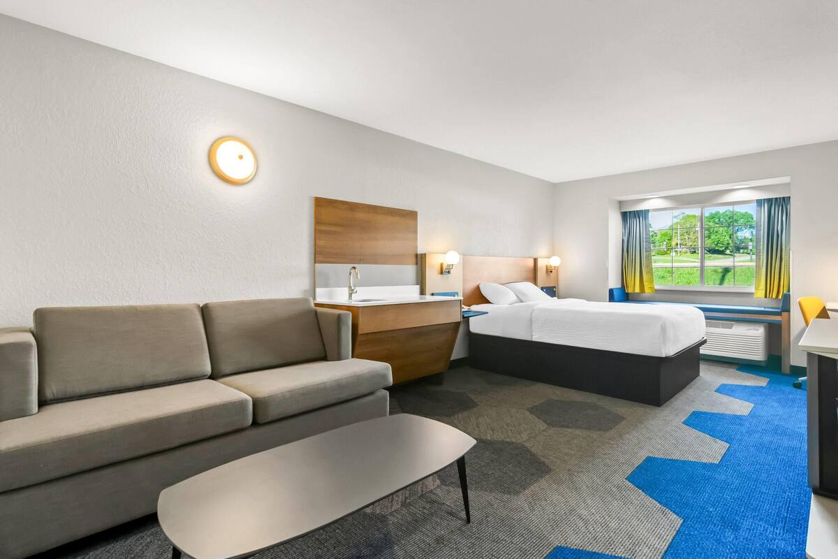 A hotel room with a sofa, a bed, a desk, a mirror, and a window with curtains.