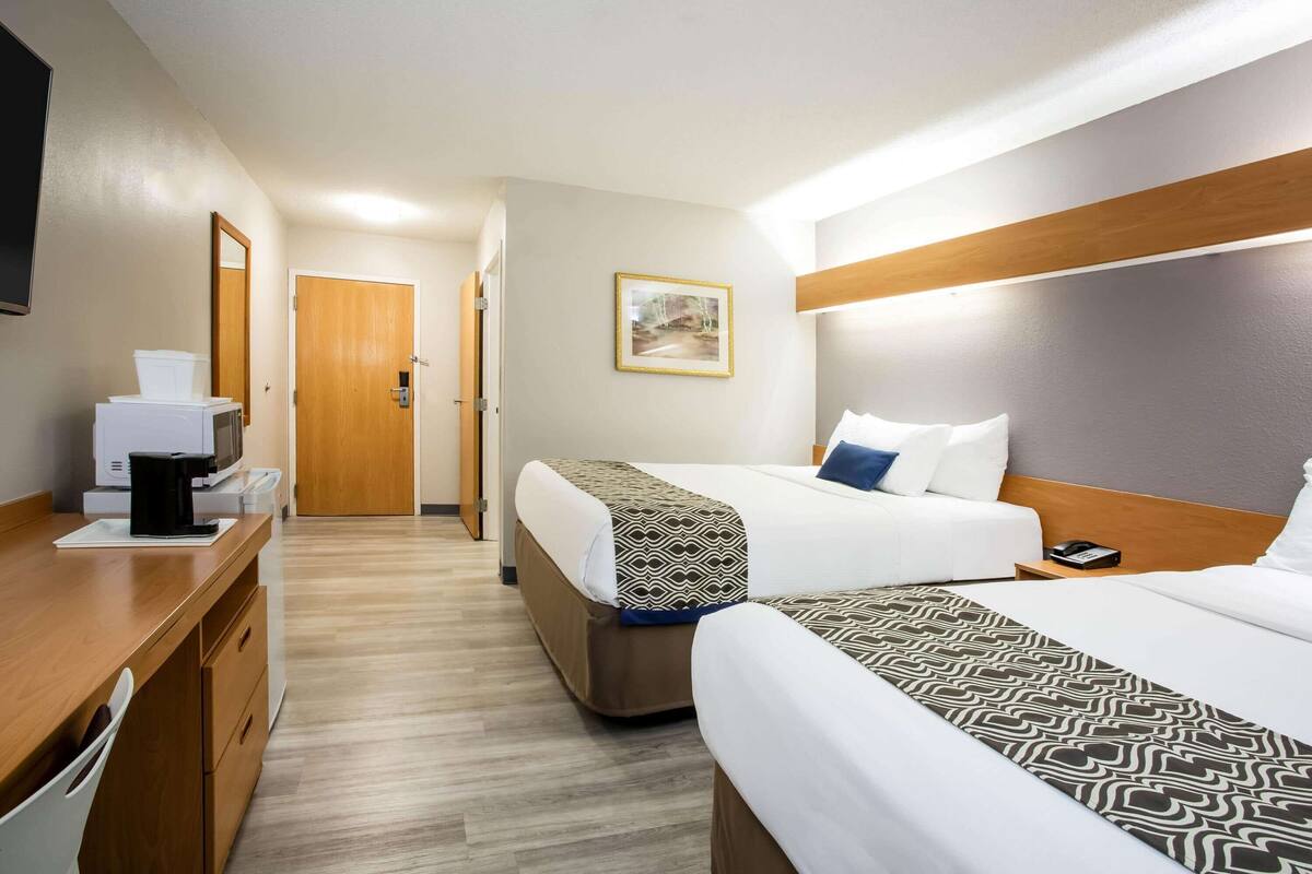 Una habitación de hotel con dos camas, un escritorio con cafetera, un espejo y un cuadro en la pared.