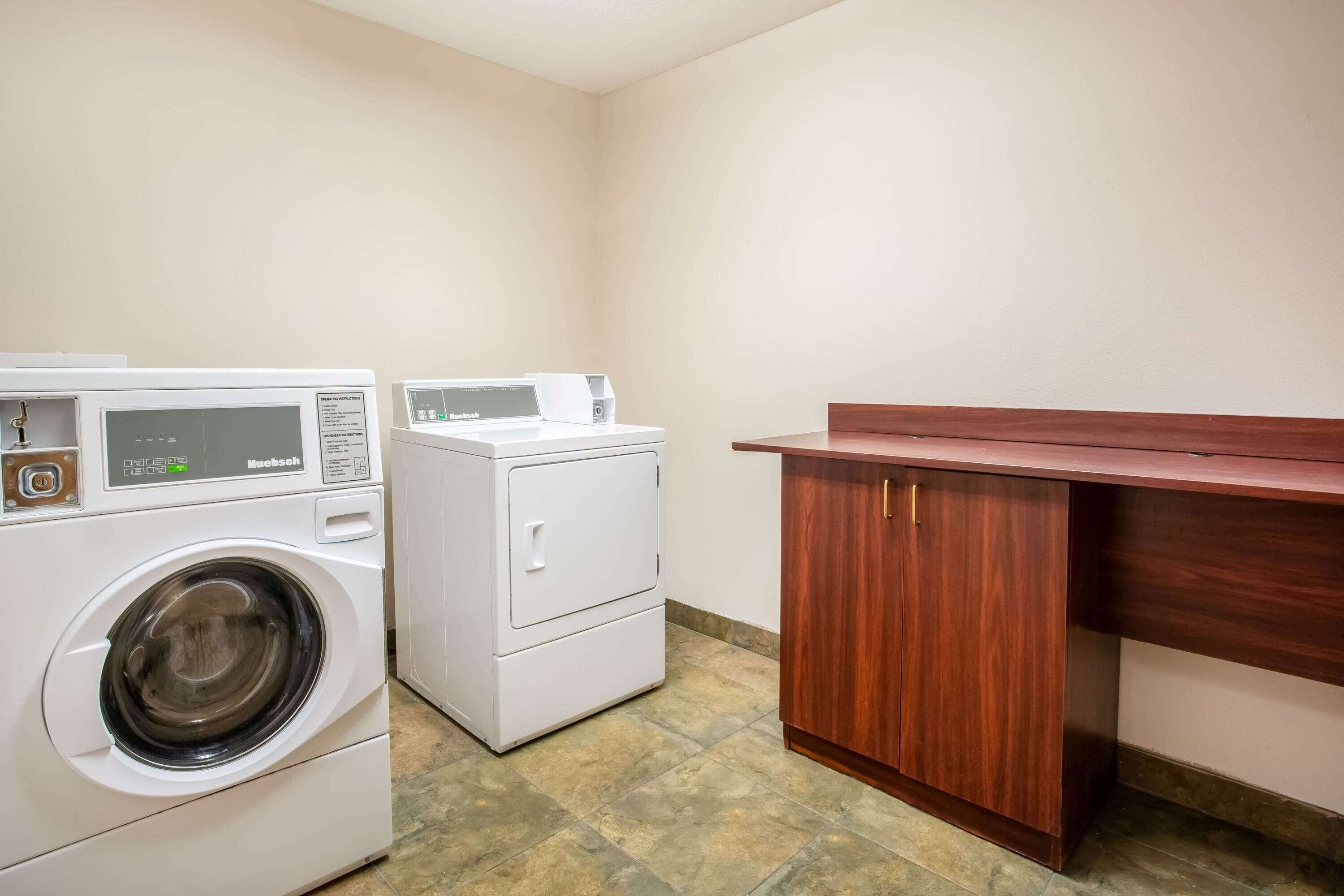A laundry room with a front-loading washing machine, a dryer, and a wooden cabinet.