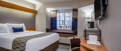A hotel room with a large bed, a desk with a chair, a television, and a window with curtains.