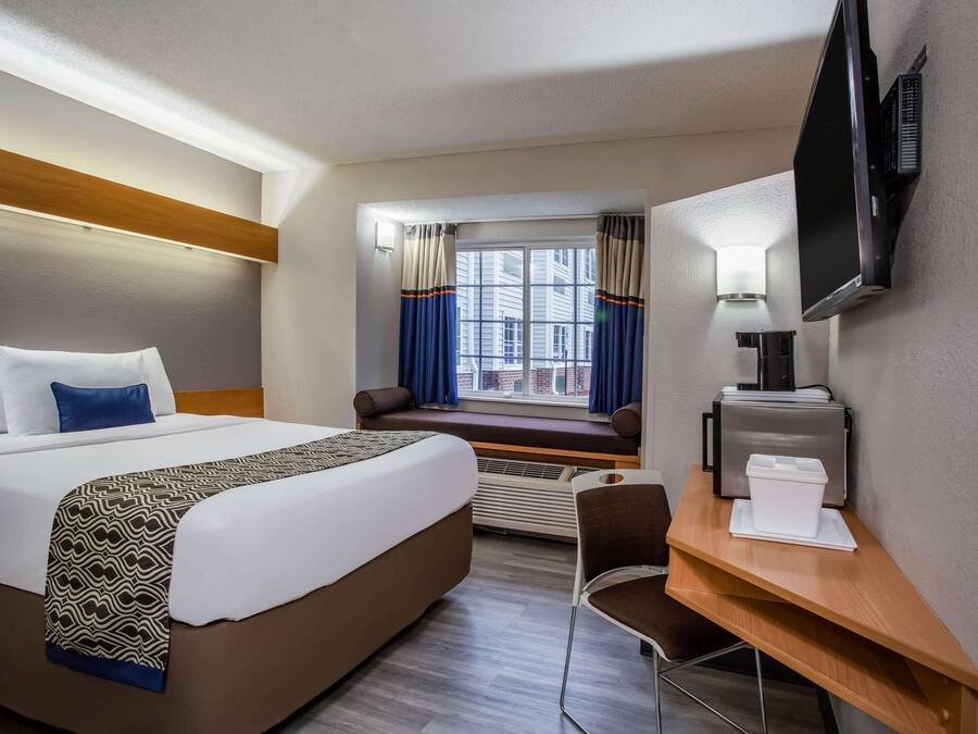 A hotel room with a large bed, a desk with a chair, a television, and a window with curtains.