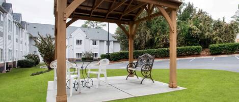 A wooden pergola with a table and chairs in a well-maintained garden area.