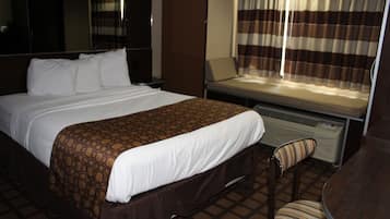 Una habitación de hotel con una cama grande, un escritorio, una silla y una ventana con cortinas.