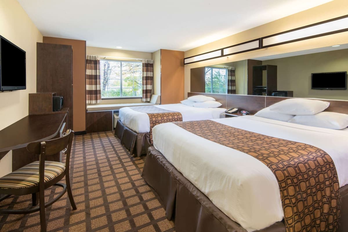 Ein Hotelzimmer mit zwei Betten, einem Schreibtisch, einem Sessel, einem Fernseher und einem Fenster mit Vorhängen.