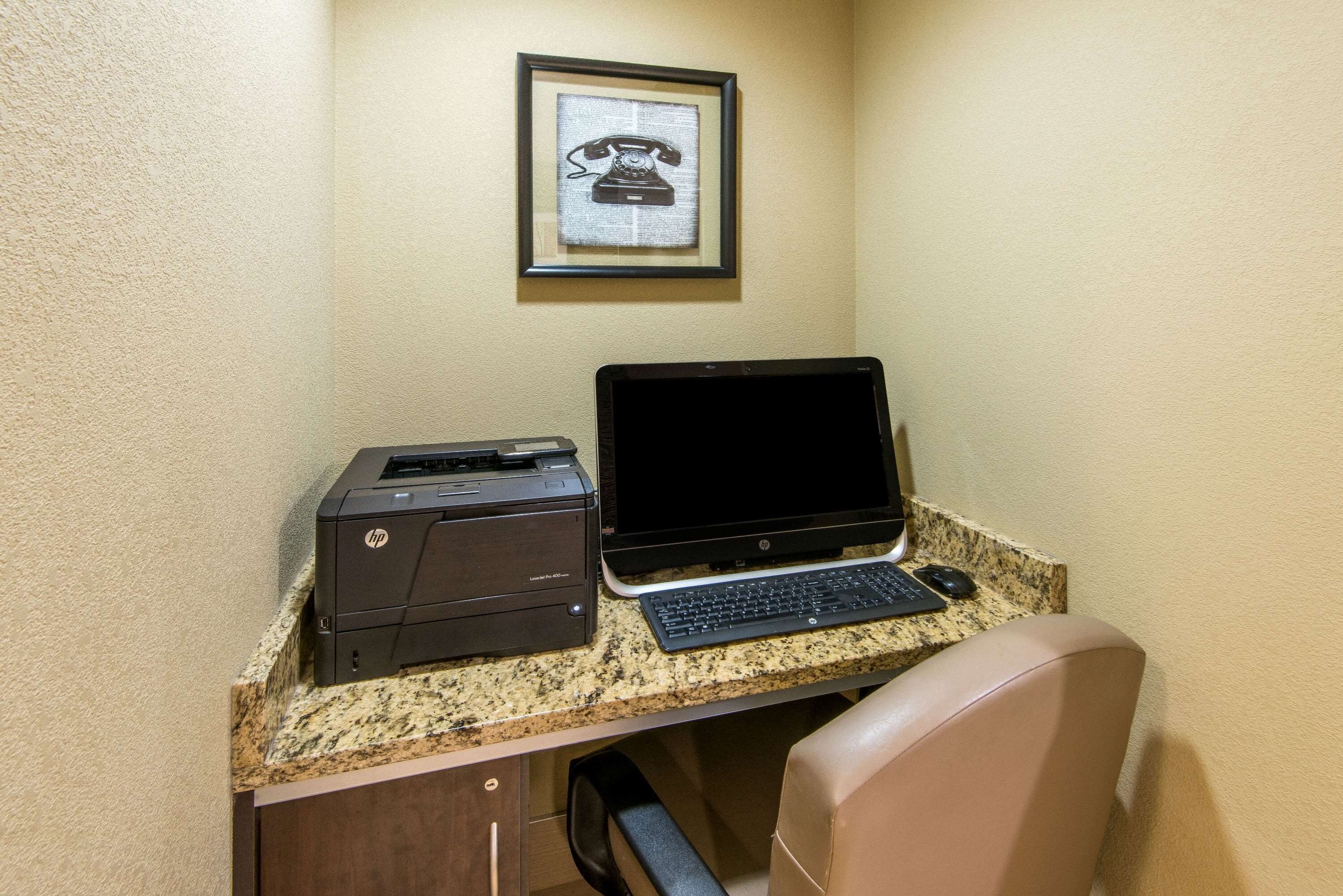 Un espacio de trabajo con una impresora HP y un ordenador portátil sobre una encimera de granito, un teléfono enmarcado en la pared y una silla de cuero marrón.