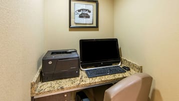 Un espacio de trabajo con una impresora HP y un ordenador portátil sobre una encimera de granito, un teléfono enmarcado en la pared y una silla de cuero marrón.