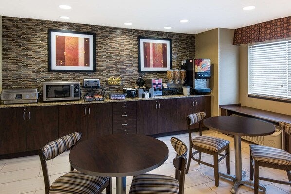 A modern kitchen with dark wood cabinets, a granite countertop, and a dining area with striped chairs and a round table. - Microtel Inn & Suites by Wyndham North Canton (North Canton)