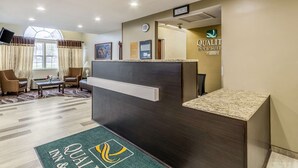 A reception area with a dark wooden desk, a clock, and a sign for 'Quality Inn & Suites'. There are two chairs and a small table with a vase of flowers. - Quality Inn & Suites North Lima - Boardman (North Lima)