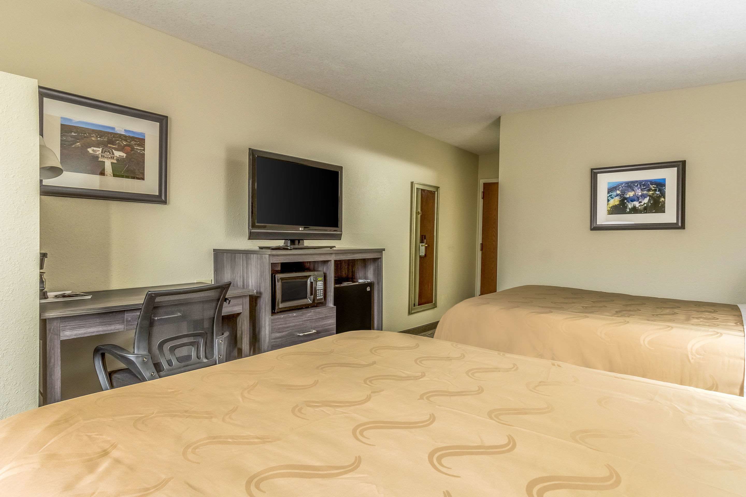 A hotel room with two beds, a desk with a television, a microwave, and a chair.