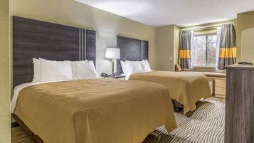 A hotel room with two beds, a desk, a lamp, and a window with curtains.