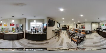 Un moderno vestíbulo de hotel con mostrador de recepción curvo, zona de estar y una gran pantalla de televisión.