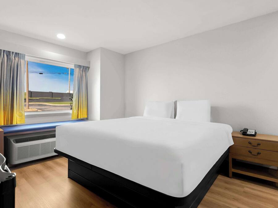 A modern hotel room with a large bed, a bedside table with a phone, and a view of the outdoors.