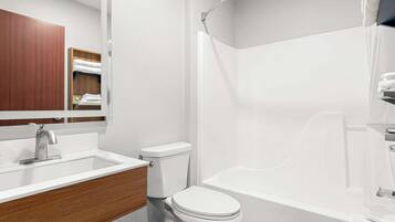 A modern bathroom with a white sink, wooden vanity, a toilet, and a bathtub.