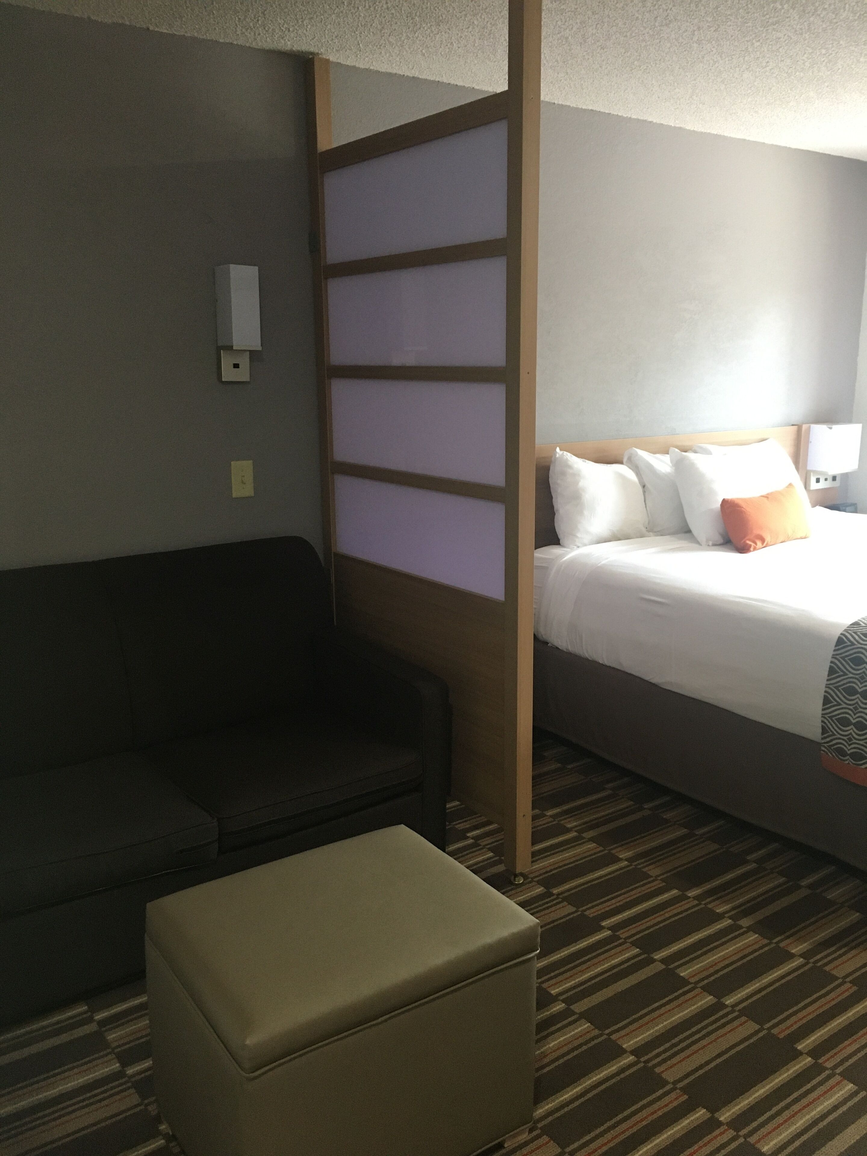A hotel room with a bed, a sofa, and a small ottoman.