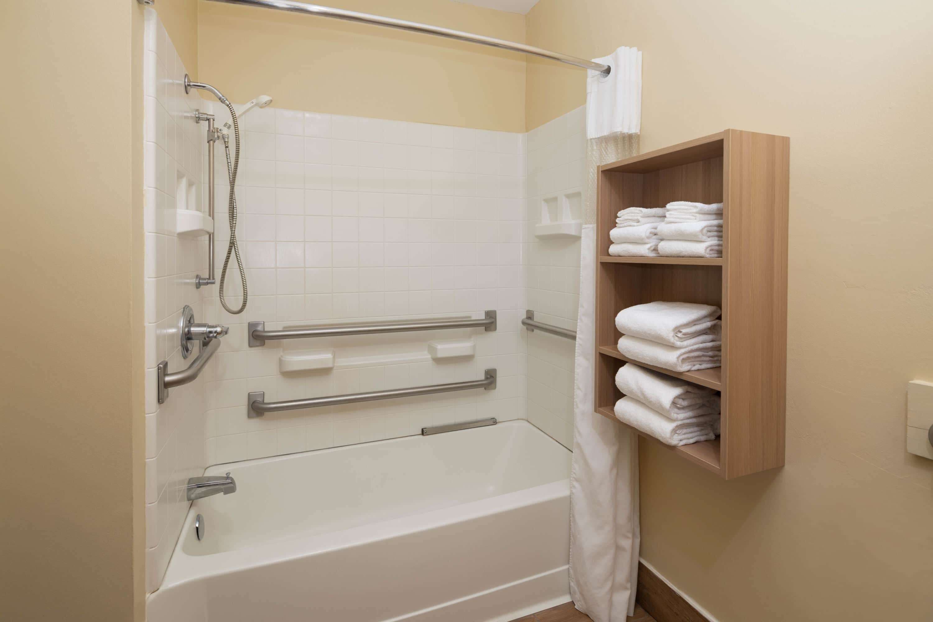 Ein Badezimmer mit Badewanne, Dusche und einem Holzregal mit Handtüchern.