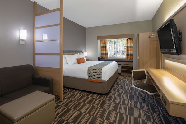 A hotel room with a bed, a desk, a chair, a television, and a window with curtains.